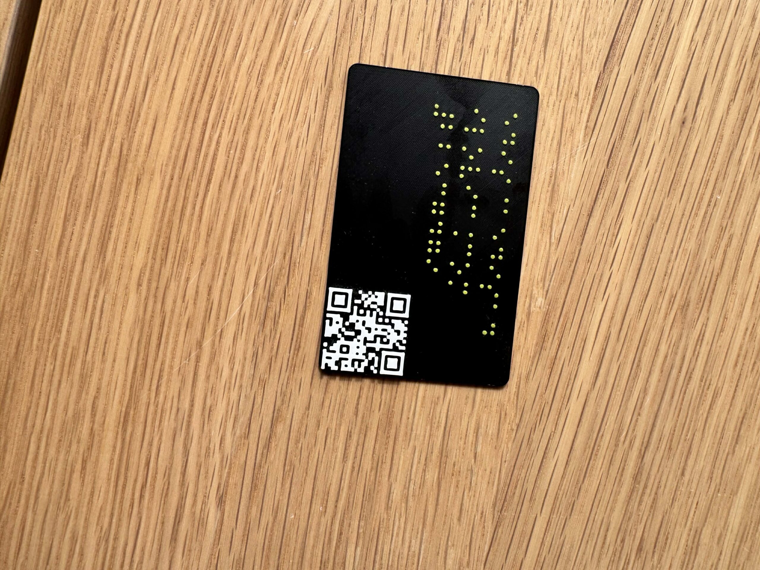 3D-printed black business card with braille and QR code on a wooden surface.